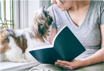 Vrouw die notities neemt in een boek, met een hond naast haar.